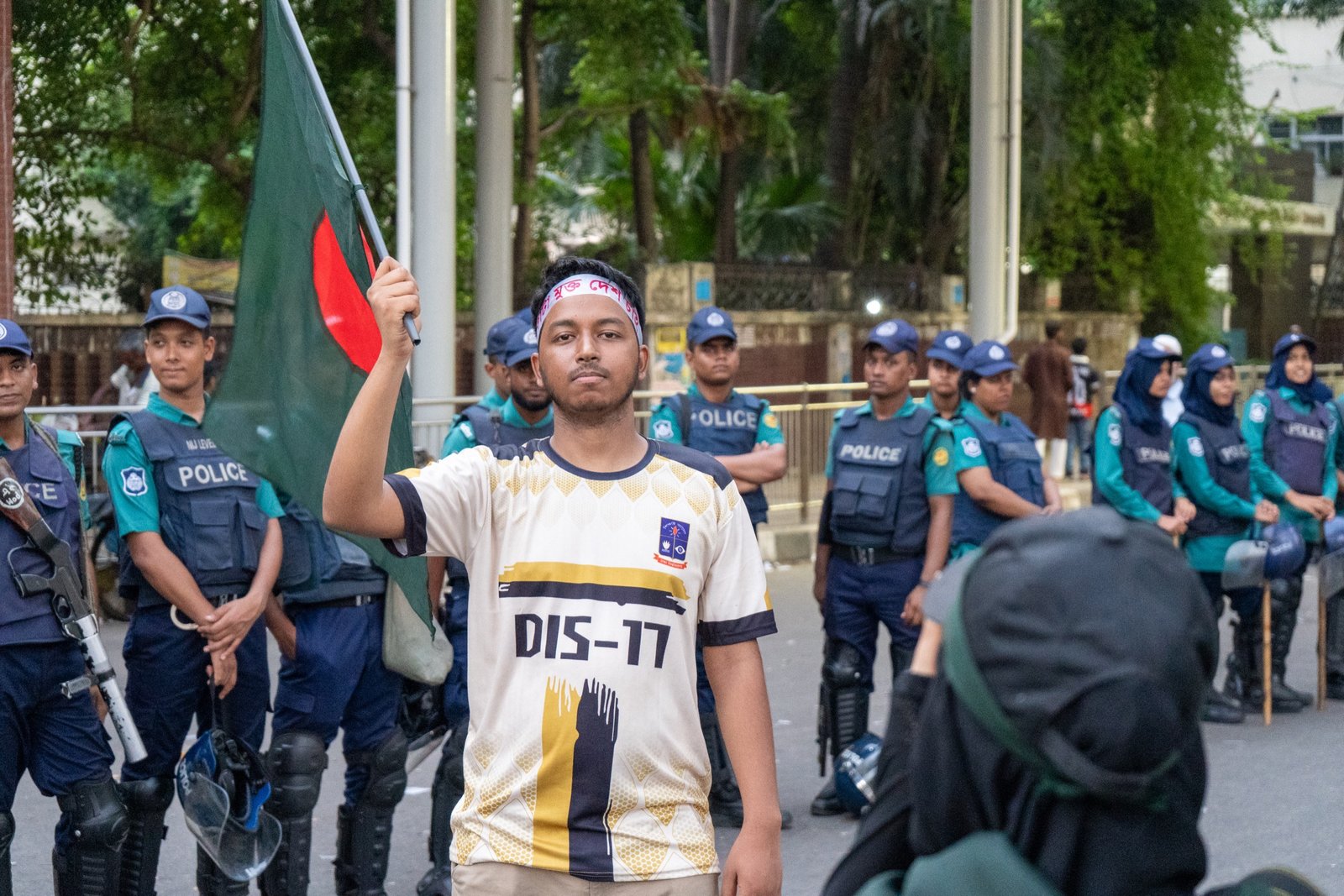 Young protester holding a Bangladesh flag in front of a police line