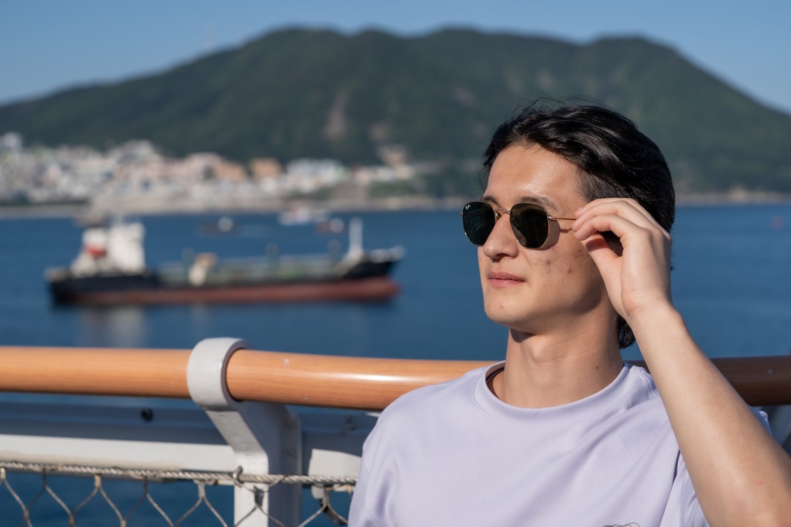 Portrait subject adjusting sunglasses with a harbor and mountain backdrop