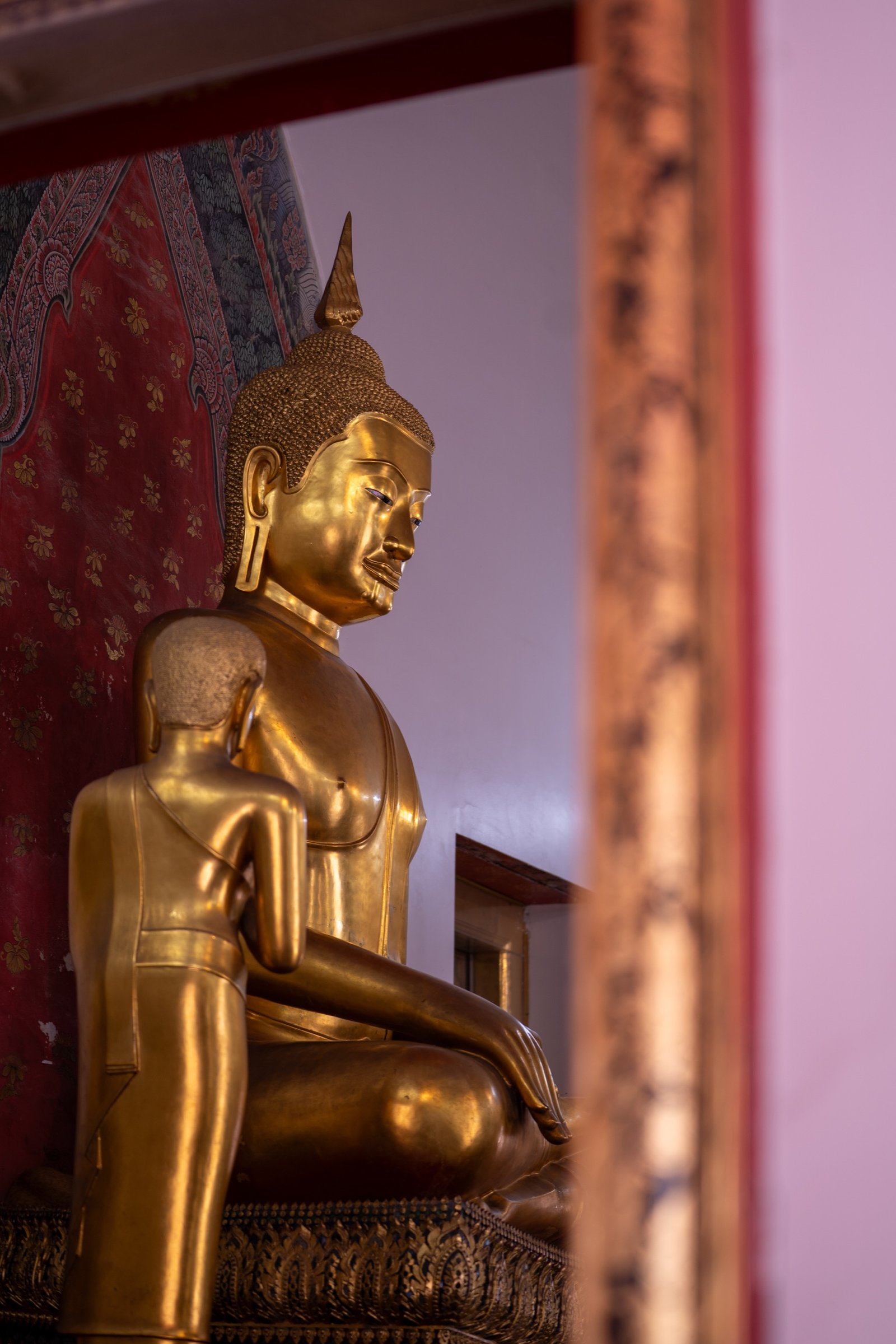 Golden seated Buddha statue framed by a red wall and doorway