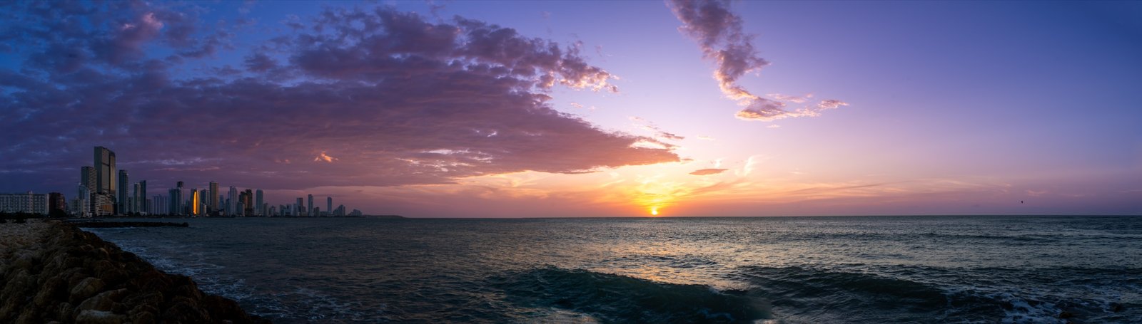 Sunset over water with a distant skyline and rolling surf