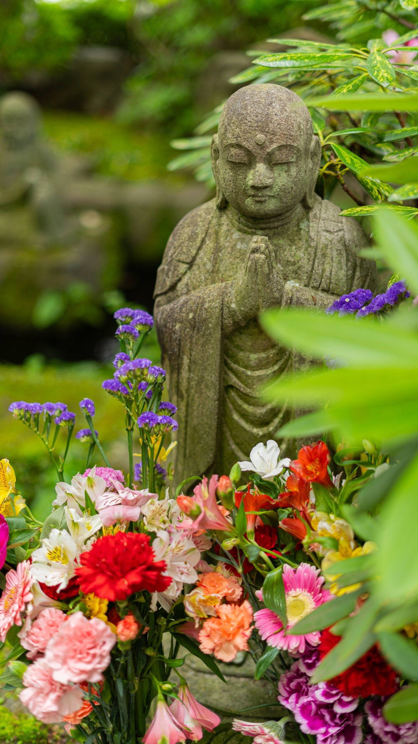 Small stone statue surrounded by flowers and greenery