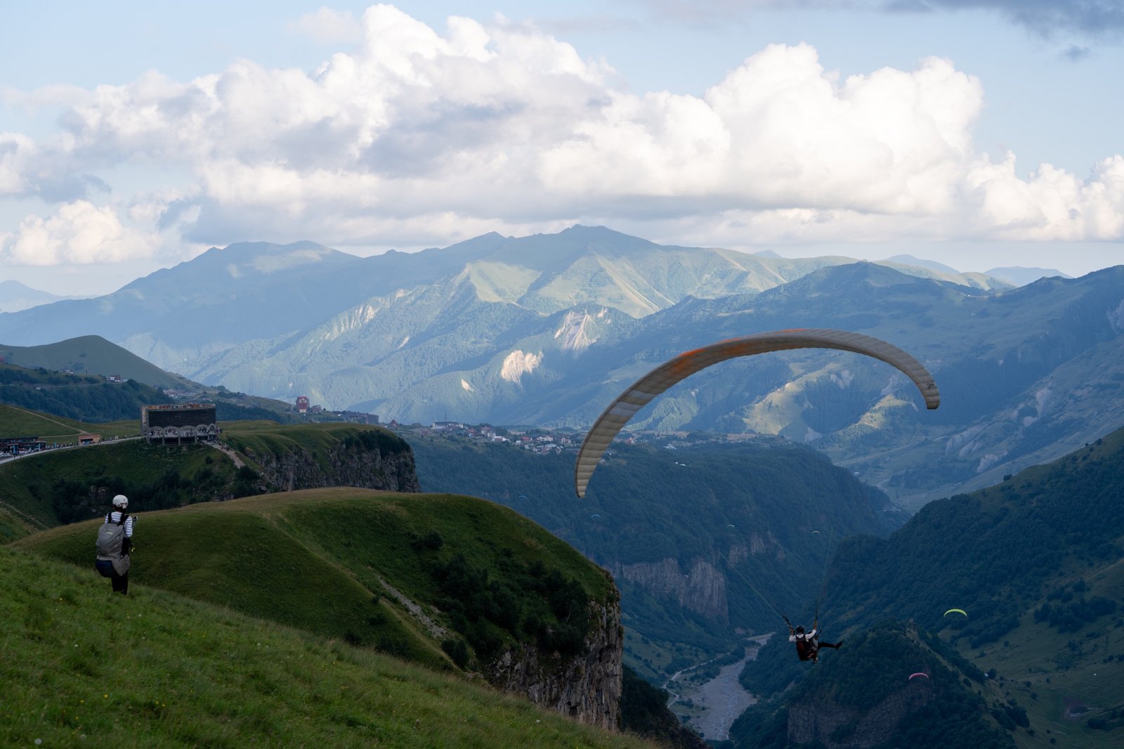 Paragliders crossing a mountain valley under wide summer clouds