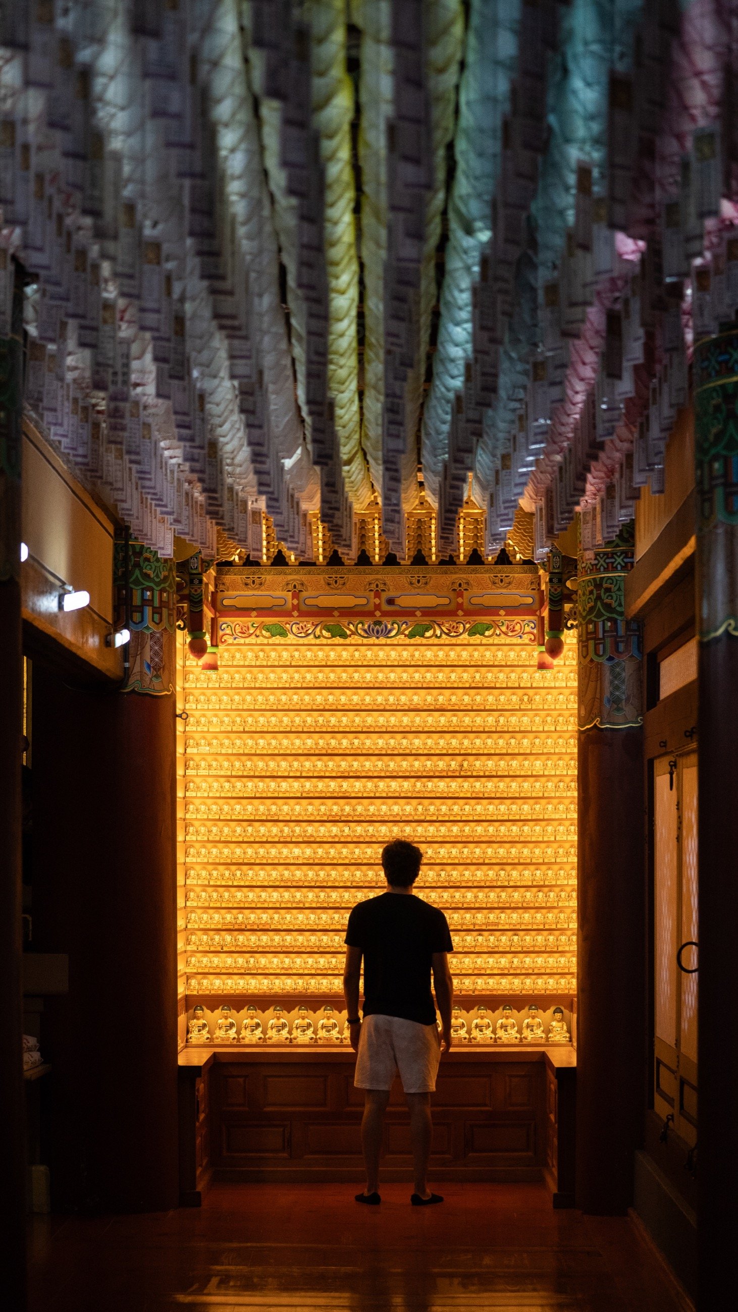Silhouette standing before a glowing wall of lanterns beneath hanging paper tags